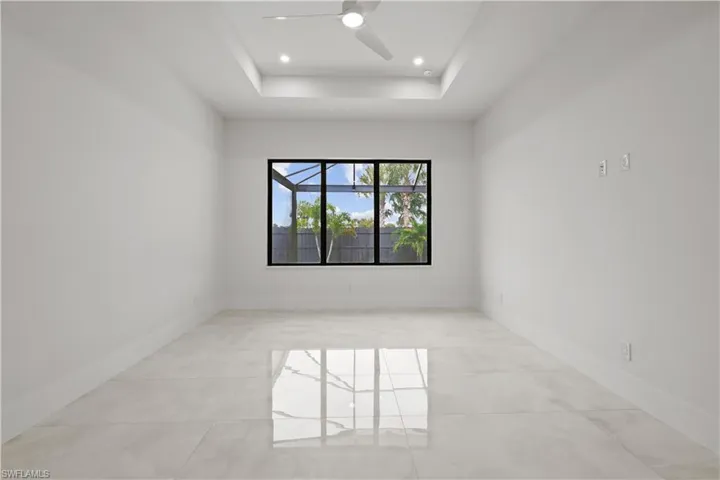 Empty room featuring a raised ceiling, ceiling fan, light tile patterned floors, and recessed lighting