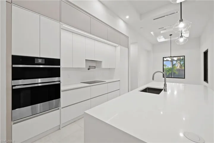 Kitchen with modern cabinets, double oven, hanging light fixtures, white cabinets, and light tile patterned floors