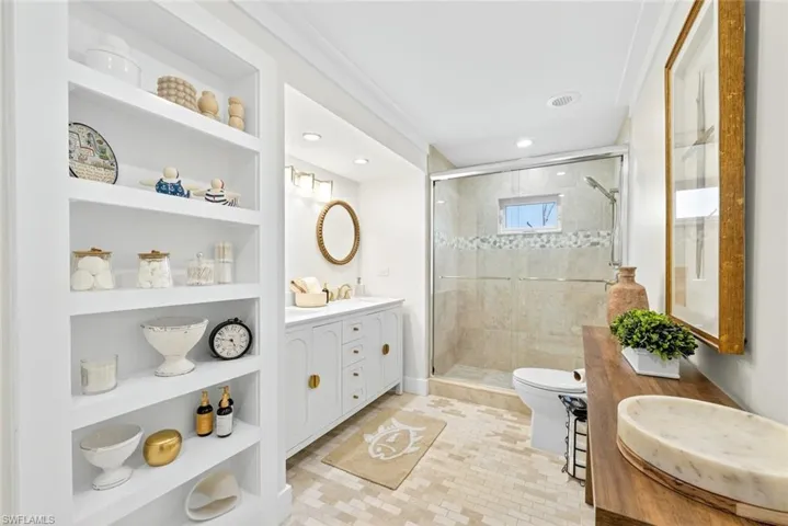Contemporary bathroom featuring built-in shelving, a dual-sink vanity with gold-tone hardware, a tiled shower enclosure with sliding glass doors, a window within the shower, and mosaic tile flooring