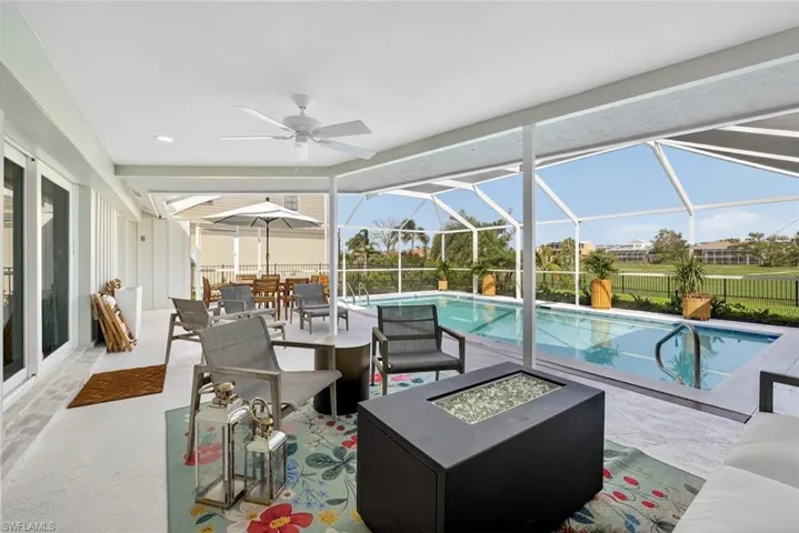 Expansive screened lanai featuring a ceiling fan, a rectangular swimming pool with integrated steps, and a decorative fire pit