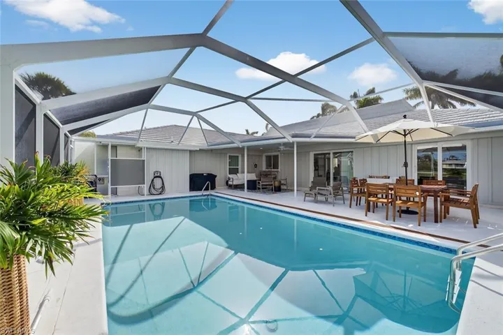 Screened pool enclosure featuring a large rectangular pool with integrated steps, a spacious paved patio, and multiple sliding glass door entries to the main residence