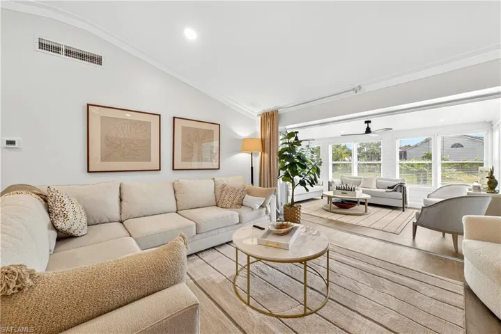 Spacious living area featuring vaulted ceilings with crown molding, wood-finish flooring, and ample natural light from multiple windows