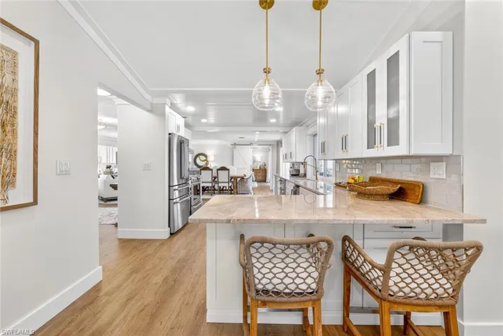 Kitchen featuring a breakfast bar with stone-finish countertop, white cabinetry with gold-tone hardware, stainless steel appliances, and wood-finish flooring