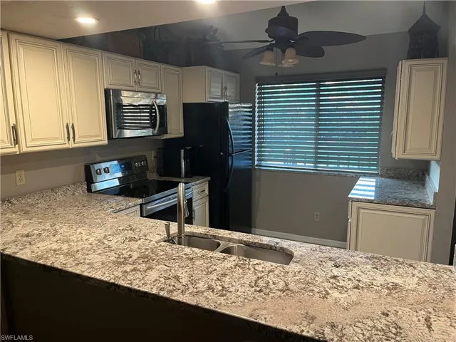 Kitchen with appliances with stainless steel finishes, light stone countertops, white cabinetry, and ceiling fan