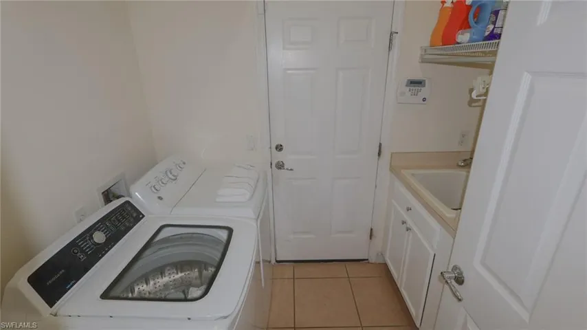 Clothes washing area with washing machine and clothes dryer, cabinet space, a sink, and light tile patterned floors