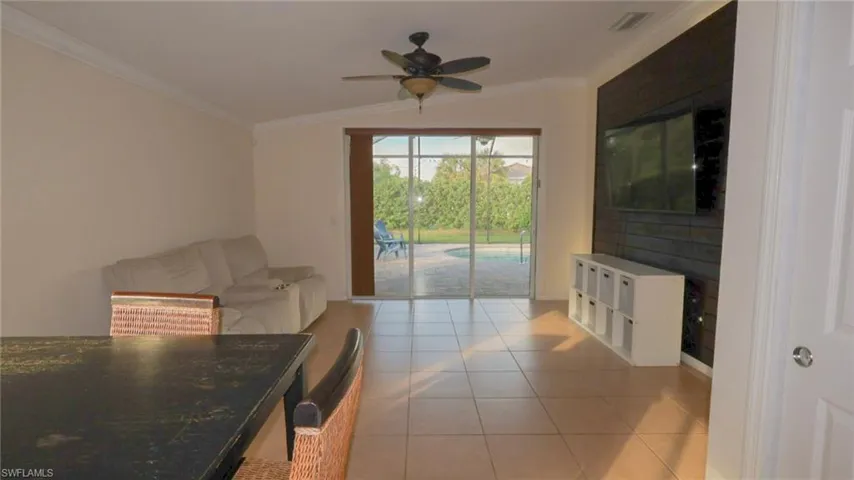 Living room featuring light tile patterned flooring, crown molding, visible vents, and ceiling fan