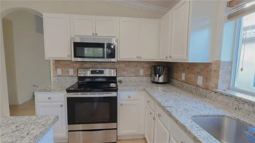 Kitchen with crown molding, light stone counters, backsplash, white cabinetry, and appliances with stainless steel finishes