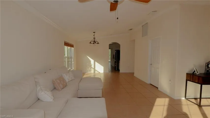 Living area featuring light tile patterned flooring, a ceiling fan, visible vents, arched walkways, and ornamental molding