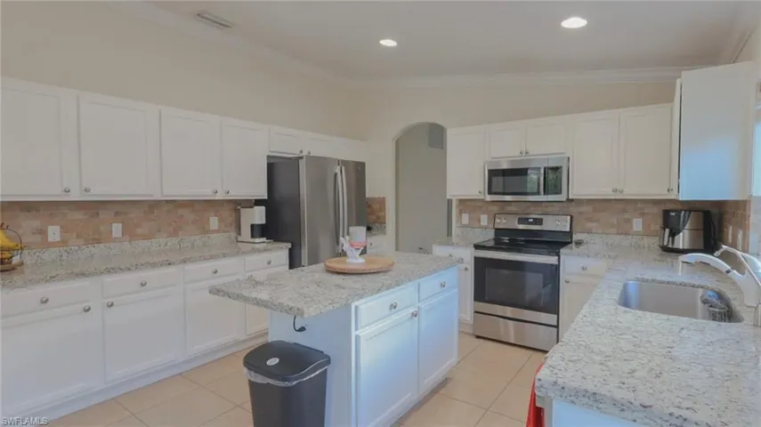Kitchen featuring light tile patterned flooring, white cabinets, stainless steel appliances, a sink, and backsplash