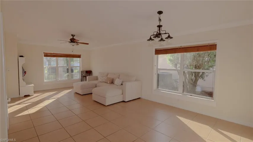 Unfurnished living room featuring light tile patterned floors, baseboards, crown molding, and ceiling fan with notable chandelier