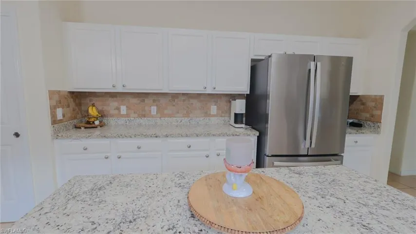 Kitchen with white cabinetry, tasteful backsplash, light stone counters, and freestanding refrigerator