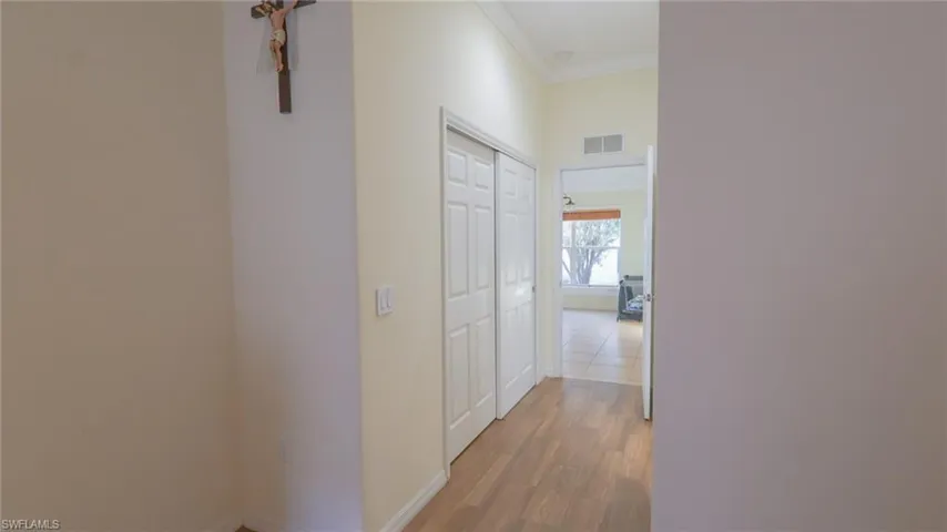 Corridor featuring baseboards, light wood-style flooring, visible vents, and ornamental molding