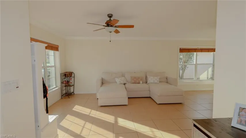 Living area with light tile patterned flooring, a wealth of natural light, ornamental molding, and a ceiling fan
