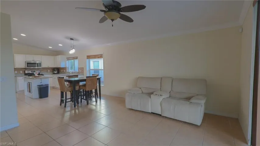 Dining area featuring light tile patterned flooring, vaulted ceiling, a ceiling fan, baseboards, and ornamental molding