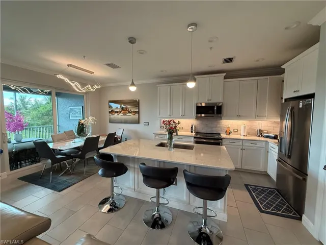 Kitchen with ornamental molding, backsplash, stainless steel appliances, white cabinets, and light stone counters