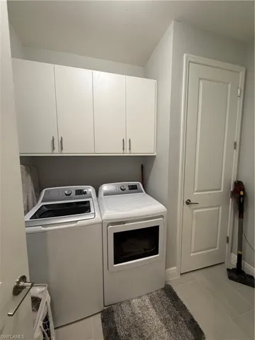 Washroom with light tile patterned flooring, cabinet space, and washer and clothes dryer
