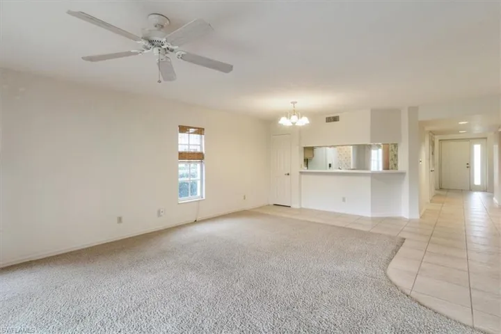 Unfurnished living room featuring ceiling fan with notable chandelier and light carpet