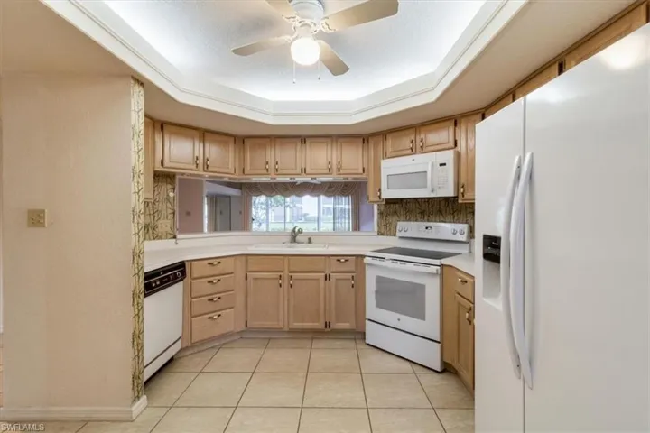 Kitchen featuring white appliances, sink, ceiling fan, a tray ceiling, and light tile patterned flooring
