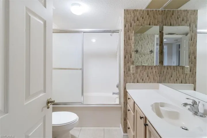 Full bathroom featuring a textured ceiling, vanity, tile patterned flooring, toilet, and enclosed tub / shower combo