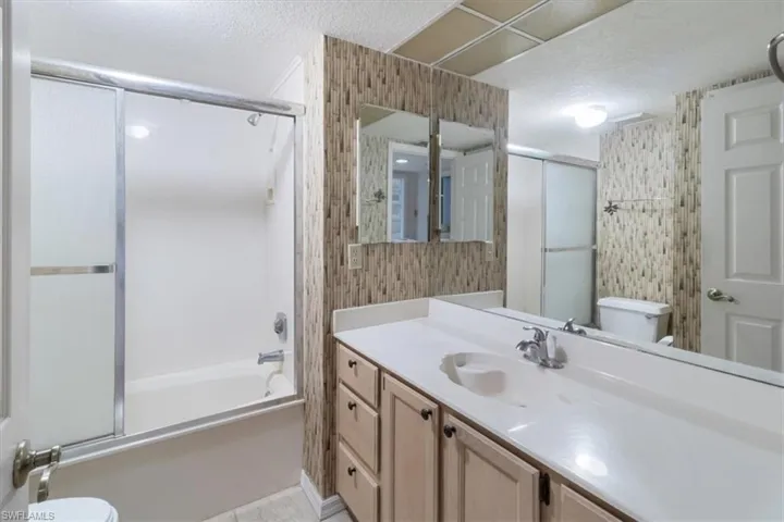 Full bathroom with toilet, a textured ceiling, combined bath / shower with glass door, and vanity