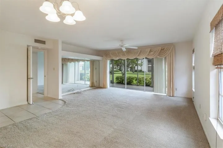 Unfurnished living room with ceiling fan with notable chandelier and light carpet
