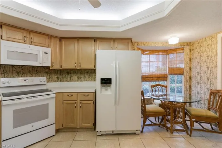 Kitchen with light brown cabinetry, light tile patterned floors, white appliances, ceiling fan, and a textured ceiling