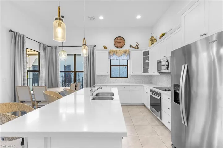 Kitchen featuring appliances with stainless steel finishes, sink, an island with sink, white cabinetry, and decorative light fixtures
