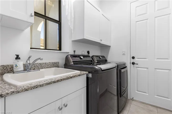 Laundry area with sink, independent washer and dryer, cabinets, and light tile patterned floors