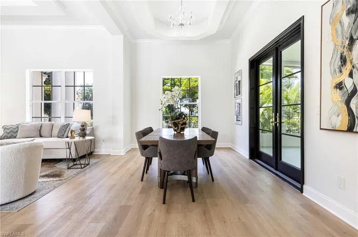 Dining room featuring french doors, crown molding, light wood-type flooring, a tray ceiling, and a notable chandelier