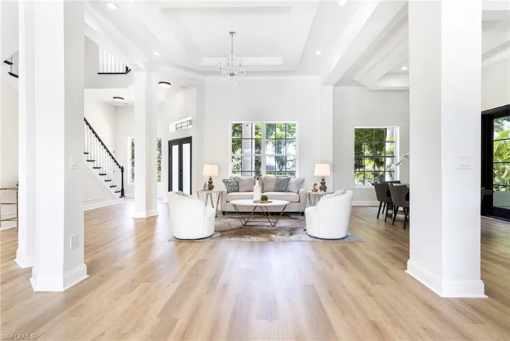 Living room with a towering ceiling, light wood-type flooring, and custom tray ceilings and wood pillars