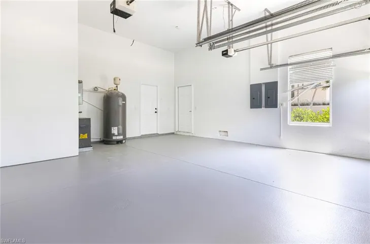 Garage featuring electric water heater, electric panel, and a garage door opener