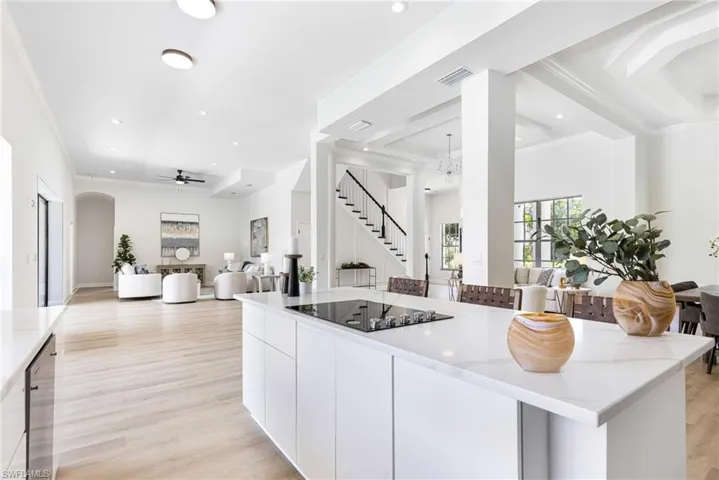 Kitchen with white cabinets, light stone counters, light wood-type flooring, ceiling fan with notable chandelier, and black electric stovetop