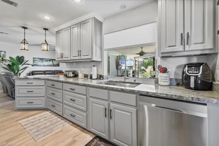Kitchen with dishwasher, a sink, light wood-style flooring, light stone counters, and gray cabinetry