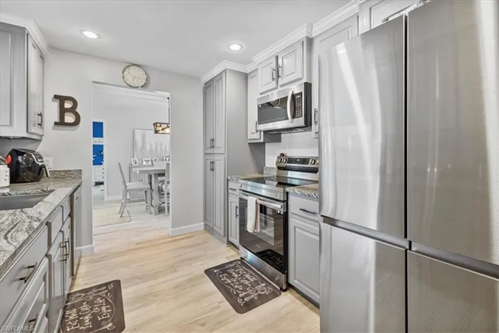 Kitchen featuring appliances with stainless steel finishes, gray cabinets, baseboards, light stone countertops, and light wood-type flooring