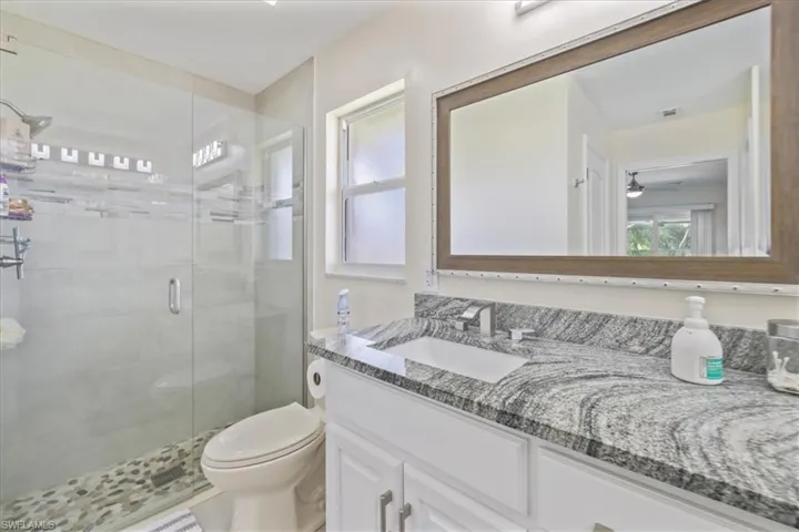 Full bath with a stall shower, toilet, vanity, and ceiling fan