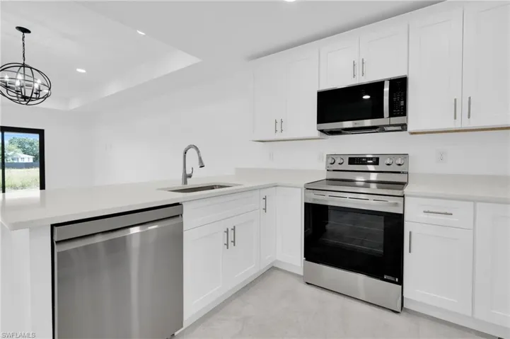 Kitchen with stainless steel appliances, white cabinets, a peninsula, light stone counters, and recessed lighting