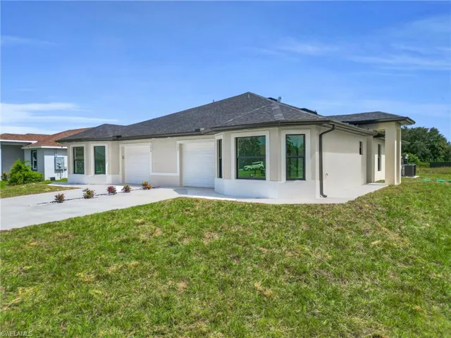 Back of house with stucco siding, a yard, driveway, and roof with shingles