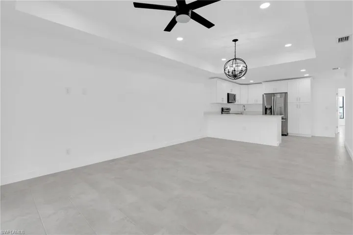 Unfurnished living room featuring a raised ceiling, recessed lighting, a chandelier, and ceiling fan