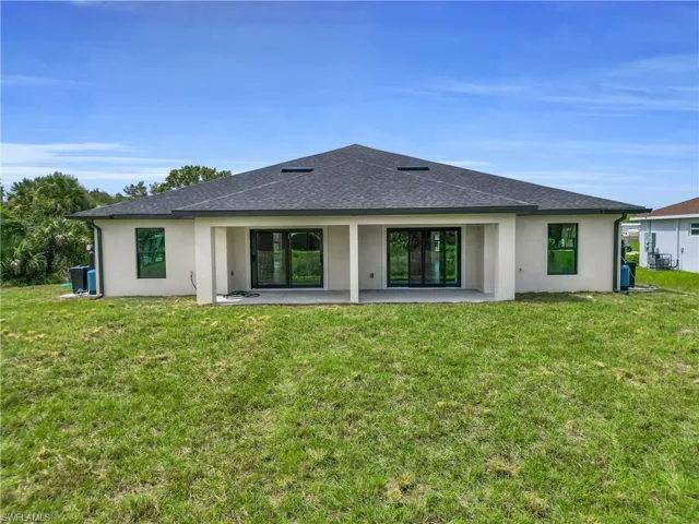 Back of property with a shingled roof, stucco siding, a patio area, and a lawn