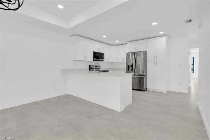 Kitchen with appliances with stainless steel finishes, white cabinetry, recessed lighting, a peninsula, and light stone countertops