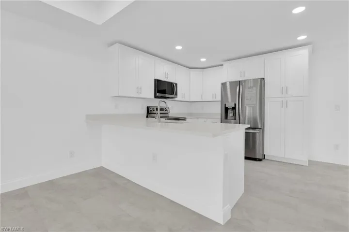 Kitchen with stainless steel appliances, recessed lighting, white cabinetry, a peninsula, and light stone counters