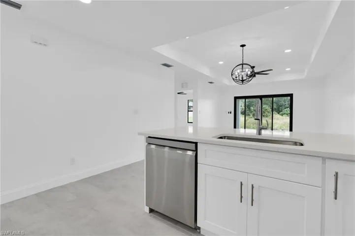 Kitchen with a raised ceiling, recessed lighting, light stone counters, dishwasher, and white cabinetry