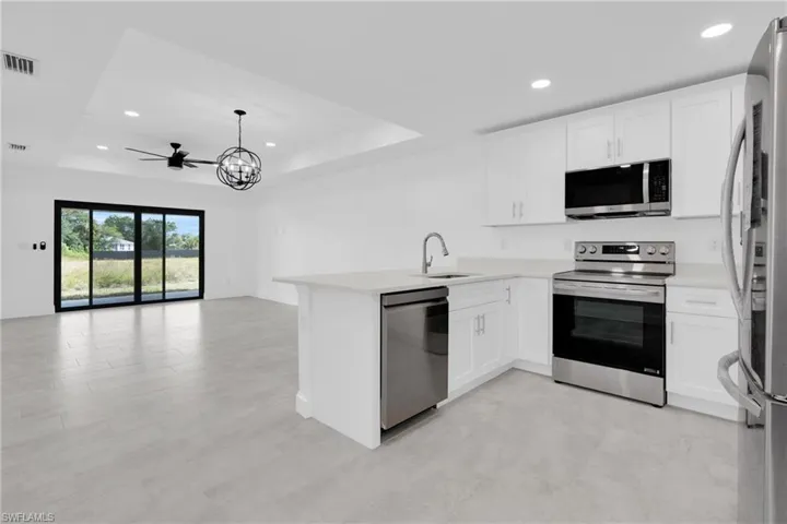 Kitchen featuring appliances with stainless steel finishes, a tray ceiling, recessed lighting, white cabinets, and a peninsula