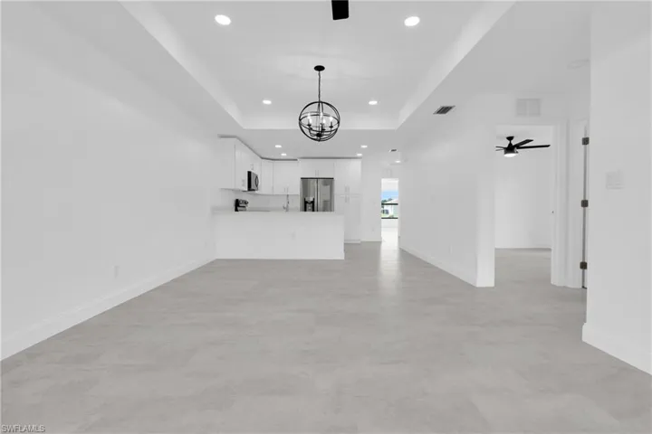 Unfurnished living room with a tray ceiling, recessed lighting, a chandelier, and ceiling fan