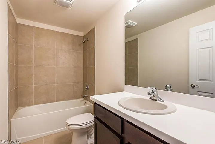 Bathroom with toilet, vanity, washtub / shower combination, and tile patterned flooring