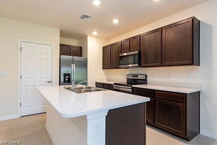 Kitchen with appliances with stainless steel finishes, a sink, dark brown cabinets, light tile patterned flooring, and baseboards