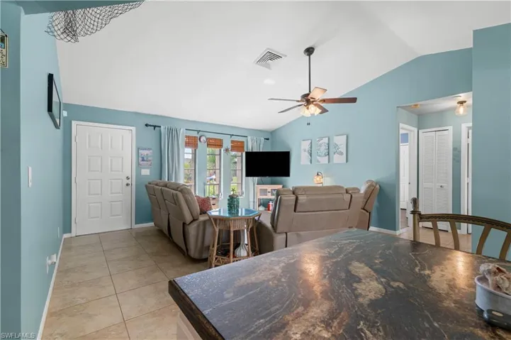 Living area with vaulted ceiling, light tile patterned flooring, and ceiling fan