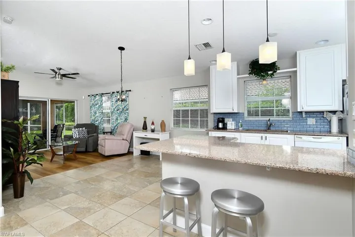 Kitchen island with granite countertop, white cabinetry, blue subway tile backsplash, and recessed lighting