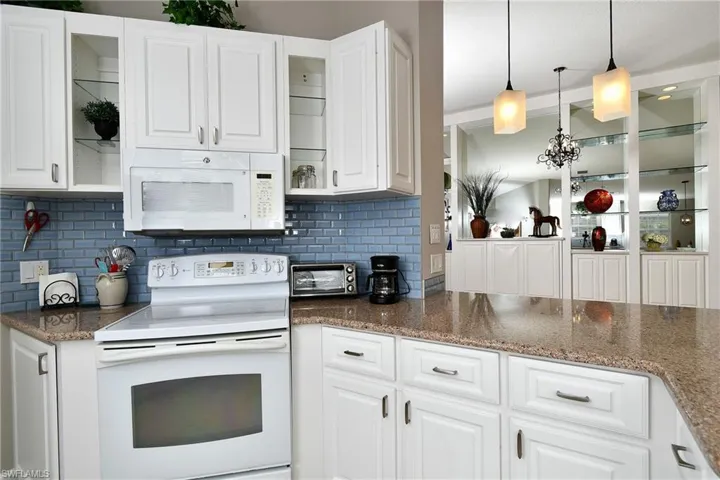 Kitchen featuring white cabinetry, blue subway tile backsplash, white appliances, and a polished countertop
