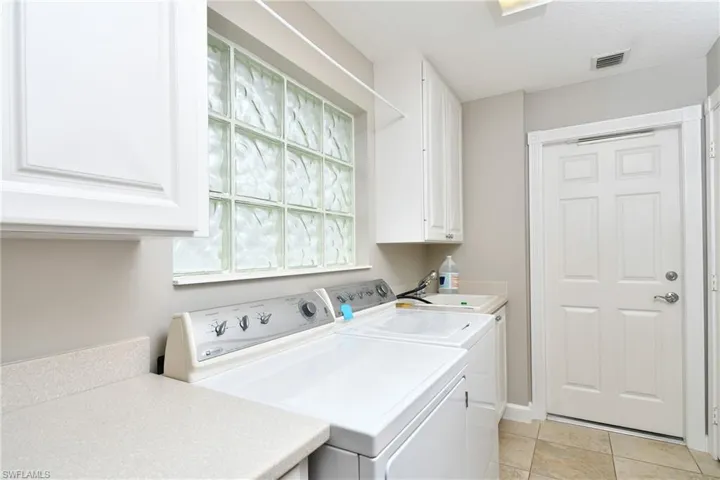 Laundry area featuring white cabinetry, a utility sink, light-toned countertop, and tiled flooring
